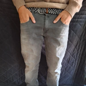 Grå jeansbyxor från Replay - Säljer ett par grå jeansbyxor från Replay Amblass med klassisk femficksdesign och normal passform. Byxorna har dragkedja och knapp framtill samt bälteshällor. Perfekta till vardags för en stilren look. W33 L32