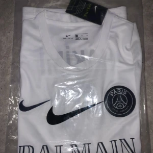 Vit PSG x Balmain fotbollströja från Nike - Snygg vit fotbollströja med Paris Saint-Germain och Balmain-logga på bröstet. Tröjan har svart Nike Swoosh och rund hals. Tillverkad i Dri-FIT material som andas. Perfekt för dig som gillar exklusiva samarbeten och stilren design.