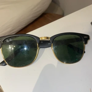 Ray-Ban Clubmaster solglasögon - Klassiska Ray-Ban Clubmaster solglasögon med svart ovandel och guldfärgade detaljer. Gröna glas och tydlig Ray-Ban-logga på sidan. Snygg retrostil som passar till många outfits. Saknas dock en ”näskudde” men det känns inte att den saknas när man har på dem