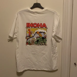 Vit t-shirt med INOHA merch - Vit t-shirt med färgglatt tryck på både bröstet och ryggen. Den är helt ny och jag säljer den för att kvaliten är kass. Själva tröjan är helt okej. Lite baggy för mig men känns bra. Den är tillverkad i bomull och är ganska tunn. Men den är en perfekt sommar tröja. Om du ej har lyssnat på INOHA borde du ta å göra det!