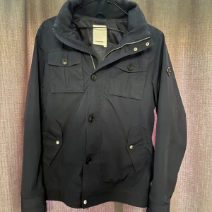 Field jacket J.Lindeberg  - Säljer nu denna snygga och stilrena jacka från J.Lindeberg | Jackan är tunnare och perfekt nu till sommaren om det är lite kallare | Jackan har en luva som har en dragkedja framför | Skick 8.5/10 har tagits väl hand om och har inga defekter | Storlek S | Hör av dig vid frågor | 