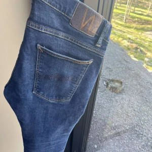 Mörkblå jeans från Nudie Jeans - Säljer ett par klassiska mörkblå jeans från Nudie Jeans med snygga kontrastsömmar och femficksmodell. Modellen grim Tim i storlek 33/32