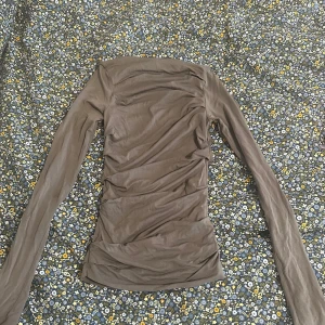 Långärmad kakifärgad boatneck topp med detaljer från Weekday - Säljer en kakifärgad långärmad från Weekday i storlek XS. Tröjan har åtsittande passform och rynkade detaljer längs sidorna. Perfekt att styla lager på lager eller som den är.  