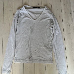 Vit ribbad långärmad tröja med v-ringning - Säljer en vit långärmad tröja med v-ringning och diskret ribbad struktur. Perfekt basplagg som är enkel att matcha till olika outfits. Mjuk och skön mot huden.