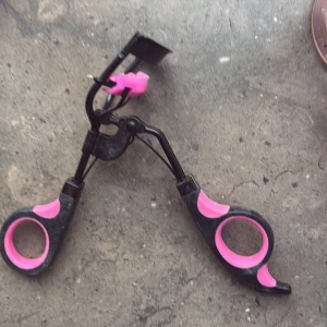 Svart och rosa ögonfransböjare som skingrar mascara så att det inte blir klumpar' - Säljer en svart ögonfransböjare med rosa detaljer. Handtaget har mjuka rosa grepp för extra komfort och böjd metallram för att forma fransarna. Perfekt för att ge fransarna en snygg böj.