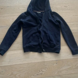 Mörkblå hoodie från U.S. Polo Assn. - Säljer en mörkblå hoodie från U.S. Polo Assn. med dragkedja och klassisk broderad logga på bröstet. Tröjan har långa ärmar, huva och två fickor framtill. Perfekt för en avslappnad stil. Dragkedja går ej att dra upp