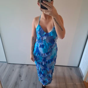 Sommar kläning - Säljer en blå långklänning med volangdetaljer i flera lager. Klänningen har ett mönster i olika blå nyanser. HELT NY