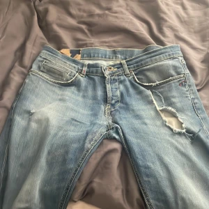  Dondup jeans  - Säljer ett par ljusblå Dondup jeans med tydliga slitningar. Klassisk femficksmodell med dragkedja och knapp. Jeansen har en slim fit och är perfekta för en vardagsstil