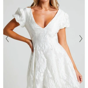 Studentklänning - Superfin vit kortklänning med puffärmar och djup v-ringning. Klänningen har ett subtilt blommigt mönster i tyget och öppen rygg. Perfekt för sommarens tillfällen och studentfirande. Säljer då jag har hittat en annan klänning till studenten, så har aldrig använts, helt i nyskick med prislapp kvar! Nypris 1200 kr säljer för 800