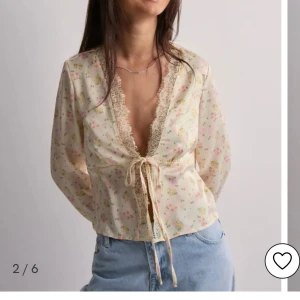 Blommig blus med spets och knytning  - Söt blommig blus i ljusbeige från Vero Moda. Spetsdetaljer längs v-ringningen och ärmsluten sen en knytning i mitten. Aldrig använd har prislappen kvar☺️