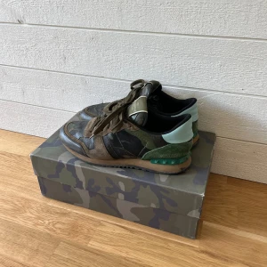 Valentino Rockrunner sneakers i camouflage - Säljer ett par Valentino Rockrunner sneakers med klassiskt camouflage-mönster i grönt, brunt och svart. Skorna har snörning, detaljer i mocka och skinn samt en unik grön häl. Kommer med originalkartong och extra skosnören. Ävkthetsbevis finns på förfrågan