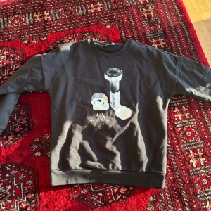 Svart sweatshirt från Armani Exchange - Cool svart sweatshirt från Armani Exchange med stort tryck av en bult och mutter på framsidan samt A|X-logga. Tröjan har rund hals och långa ärmar. Perfekt för en avslappnad och trendig stil.