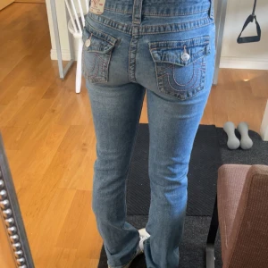 Mid-rise bootcut jeans True Religion - Säljer ett par blå bootcut jeans från True Religion med rosa detaljer på bakfickorna.💞 de enda defekten är ett litet hål vid sidan av ena fickan som syns först när man drar ut byxan som på bilden, men inget som man ser alls när man bär dem😇 skriv vid fler funderingar eller frågor!💞 