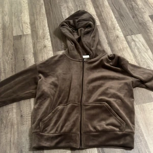 Brun fleecehoodie från H&M - Mysig brun hoodie från H&M i mjuk fleece med dragkedja framtill och två stora fickor. Perfekt för att hålla värmen under kyliga dagar. Huva och långa ärmar med muddar ger extra komfort.