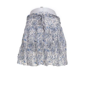 Blommig kortkjol från H&M - Söt kortkjol från H&M med blått och vitt blommönster. Kjolen har en knytning i midjan och är tillverkad i ett lätt och luftigt material, perfekt för varmare dagar.