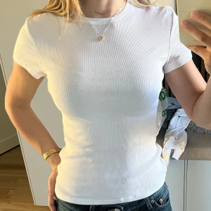 Vit ribbad t-shirt - Säljer en klassisk vit ribbad t-shirt med tight passform och korta ärmar. Perfekt basplagg som funkar till det mesta och är superenkel att styla med jeans eller kjol.