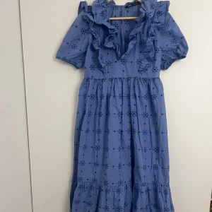 Blå klänning med volang och broderade blommor - Supersöt blå klänning med broderade blommor och volangdetaljer vid axlar och halsringning. Köpt på Zara och tyvärr aldrig använd💙den är absolut flowy och passar större storlekar också