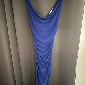 Blå långklänning med drapering från Zara - Säljer en blå långklänning från Zara med v-ringad fram- och baksida samt snygg drapering längs hela klänningen. Klänningen har smala axelband och en elegant, figurnära passform. Perfekt för dig som vill sticka ut.