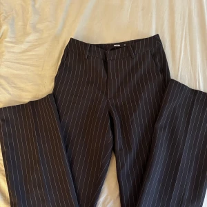 Svarta kostymbyxor med vita ränder från bikbok - Säljer ett par svarta kostymbyxor med tunna vita ränder. Dom är högmodjade och en ganska tajt passform. Storlek 34(xs). Knappt använda.
