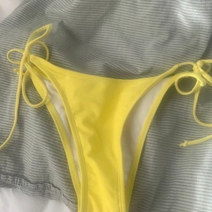 Gul bikiniunderdel  - Snygg bikiniunderdel i klar gul färg med knyt i sidorna. Modellen har en klassisk passform och är perfekt för strand eller pool. Materialet känns mjukt och följsamt mot huden.