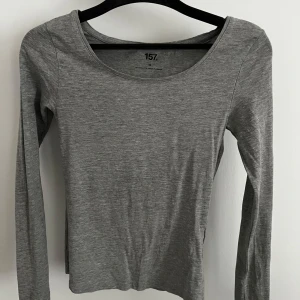 Grå långärmad topp från 157 - En enkel och stilren grå långärmad topp från 157. Modellen har rund halsringning och är tillverkad i ett mjukt och stretchigt material som sitter skönt på kroppen. Perfekt att matcha med jeans eller kjol.