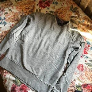 Grå sweatshirt från Tommy Hilfiger - Säljer en klassisk grå sweatshirt från Tommy Hilfiger i modellen Vintage Fit. Tröjan har rund halsringning och en liten broderad logga på bröstet. Perfekt för en avslappnad och stilren look.