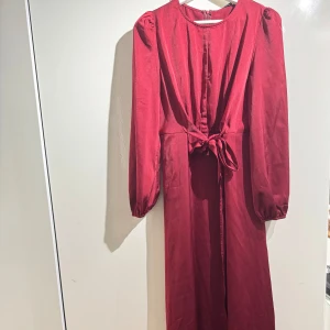 Röd långklänning med knytband - Snygg röd långklänning med långa ärmar och knytband i midjan. 