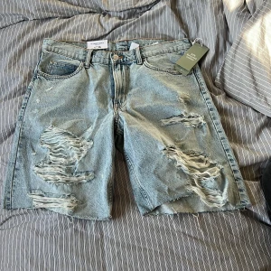 90's Baggy Shorts från H&M - Baggy jeansshorts i ljusblå denim med slitna detaljer och råa kanter. Klassisk femficksmodell med gylf och knapp. Perfekta för en avslappnad stil. Säljes pga jag har för feta lår :)