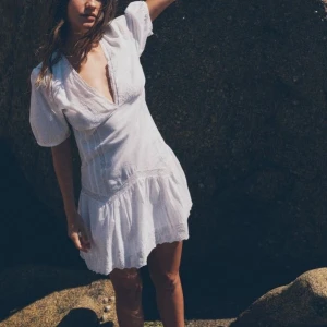 Zara klänning - Superfin vit kortklänning med v-ringning och puffärmar. Klänningen har volang nertill och är tillverkad i ett lätt bomullstyg, perfekt för varma dagar. Den har en feminin passform och fina broderade detaljer längs fållen.