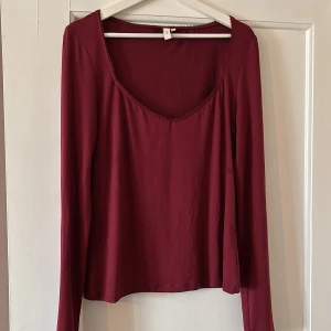 Vinröd långärmad topp från Nelly - Säljer en vinröd långärmad topp från Nelly med rundad, något djupare ringning och dekorativ kant. Tunn och mjuk i materialet, perfekt för lager-på-lager eller som den är.
