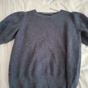 Grå stickad tröja från Vero Moda - Mysig grå stickad tröja från Vero Moda med puffärmar och rund halsringning. Perfekt för kyligare dagar och enkel att matcha med olika outfits. Ribbstickad vid ärmslut och nederkant.