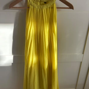 Gul plisserad klänning - Säljer en solgul plisserad klänning med hög halsringning. Klänningen har ett luftigt och flowy tyg som ger en snygg siluett. Perfekt för dig som vill sticka ut med färg och stil.