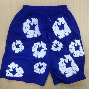 Denim tears shorts blå  - Snygga blå shorts med vita blommiga mönster över hela tyget. Shortsen har resår i midjan och snörning för extra komfort. Perfekta för sommardagar och har en bakficka. Materialet känns lätt och luftigt.