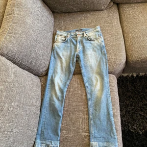 Ljusblå jeans från Nudie Jeans - Säljer ett par ljusblå jeans från Nudie Jeans med klassisk femficksdesign och snygga broderade detaljer på bakfickorna. Jeansen har raka ben och normal passform, perfekta till vardagslooken.