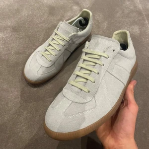 Maison Margiela Gat Suede sneakers - Säljer ett par ljusgrå Maison Margiela Gat Suede sneakers med ovandel i mocka och klassisk gummisula. Skorna har snörning och en stilren, minimalistisk design som passar till många outfits.