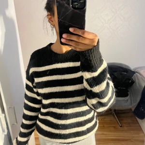 Svartvit randig stickad tröja - Mysig stickad tröja med breda svarta och vita ränder. Tröjan har lång ärm och rund halsringning, perfekt för kyligare dagar. Passformen är normal och materialet känns mjukt och bekvämt.