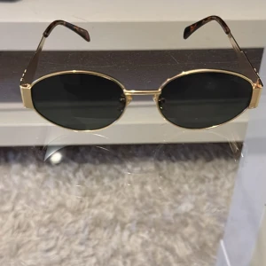 Celine guldiga ovala solglasögon - Snygga solglasögon från Celine med tunna, ovala glas och guldfärgade metallbågar. Skalmarna har sköldpaddsmönstrade ändar och Celines logga i guld på sidorna. Perfekt accessoar för att lyfta din stil med en lyxig touch.