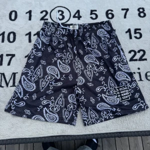 Svarta paisley shorts från Eric Emanuel - Svarta meshshorts från EE med vit paisley-mönster och broderad logga på benet. Elastisk midja med vit snörning för skön passform. Perfekta för sommaren och streetwear-stil.