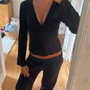 Svart knyttopp från Gina Tricot - Säljer en svart topp med knyt i ryggen från Gina Tricot i storlek XS. Toppen har lång ärm, v-ringning och knyt i ryggen. Materialet är lätt ribbat och ger en snygg passform. Perfekt till dig som gillar stilrena och enkla plagg.