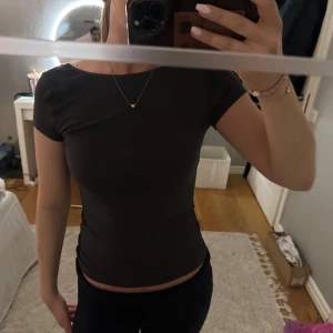 Svart croppad t-shirt med öppen rygg - En svart croppad t-shirt med korta ärmar och rund halsringning. Toppen har en snygg öppen rygg som ger en extra detalj. Perfekt till jeans eller kjol för en stilren look.