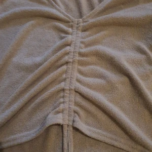 Beige croppad topp med knyt - Trendig beige croppad topp med v-ringning och kort ärm. Toppen har snygg knyt- och rynkdetalj framtill som ger en cool look. Perfekt att matcha med jeans eller kjol för en avslappnad stil.