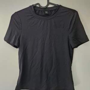 Svart tight t-shirt från Shein I storlek S - En enkel svart t-shirt från Shein i storlek S med rund halsringning och korta ärmar. Modellen är tight och tillverkad i en mjuk blandning av polyester och elastan, vilket ger en stretchig och bekväm passform.