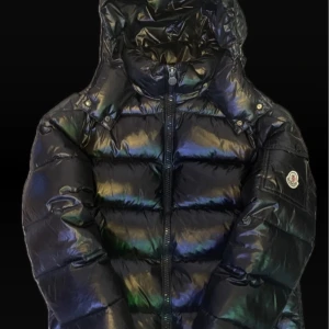 Moncler maya - Storlek 2 så S/M.                                            Moncler Maya Short Down Jacket A modern icon reimagined—crafted from Moncler’s signature glossy nylon laqué and insulated with premium goose down, the Maya delivers exceptional warmth in a sleek, urban silhouette. Featuring classic boudin quilting, a detachable hood, and the iconic logo patch, it’s the perfect fusion of alpine heritage and city-ready style. 