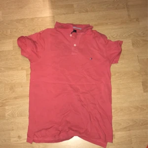 Rosa pikétröja från Tommy Hilfiger - Säljer en klassisk rosa pikétröja från Tommy Hilfiger med liten logga på bröstet och två knappar vid kragen. Perfekt för en avslappnad och stilren look.