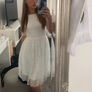 Studentklänning - Superfin vit klänning i spets med halvlånga ärmar och vacker öppen rygg. Använd en gång vid skolavslutning. Har lite smink på halsen innanför men inget som syns utuifrån! 