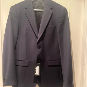 Mörkblå kavaj från SIR, August Jacket - Stilren mörkblå kavaj från SIR, modell August Jacket. Klassisk passform strl 46=M  Materialet är mjukt och följsamt. Pris ej hugget i sten. Aldrig använd!