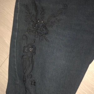 Mörkblå Max & Liu jeans med broderi - Snygga mörkblå jeans från Max & Liu med unika svarta blombroderier på framsidan, väldigt y2k. Byxorna sitter som en bootcut och jag skulle säga är storlek M/L även fast dwt stårXL