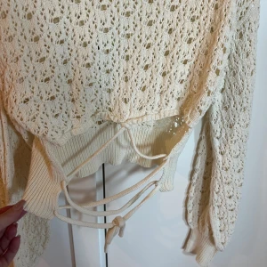 Cremefärgad spetsstickad tröja med snörning i ryggen från Pull&Bear - Supersöt cremefärgad spetsstickad tröja från Pull&Bear med långa ärmar och snygg snörningsdetalj i ryggen. Perfekt för dig som gillar romantisk stil och vill ha något unikt i garderoben. 💫