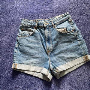 Blå högmidjade jeansshorts H&M Divided - Snygga blå jeansshorts från H&M Divided i klassisk modell med hög midja och uppvikta benslut. Shortsen har fem fickor och bälteshällor, perfekta för sommardagar. Tillverkade i 100% bomull för en skön och avslappnad känsla.