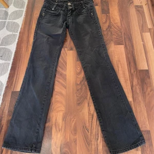 Svarta jeans låg midja - Säljer ett par svarta manchesterbyxor från Wrangler i klassisk modell med raka ben och fem fickor. Byxorna har normal passform och snygga detaljer med knappar och broderade bakfickor. Perfekta för dig som gillar tidlös stil.